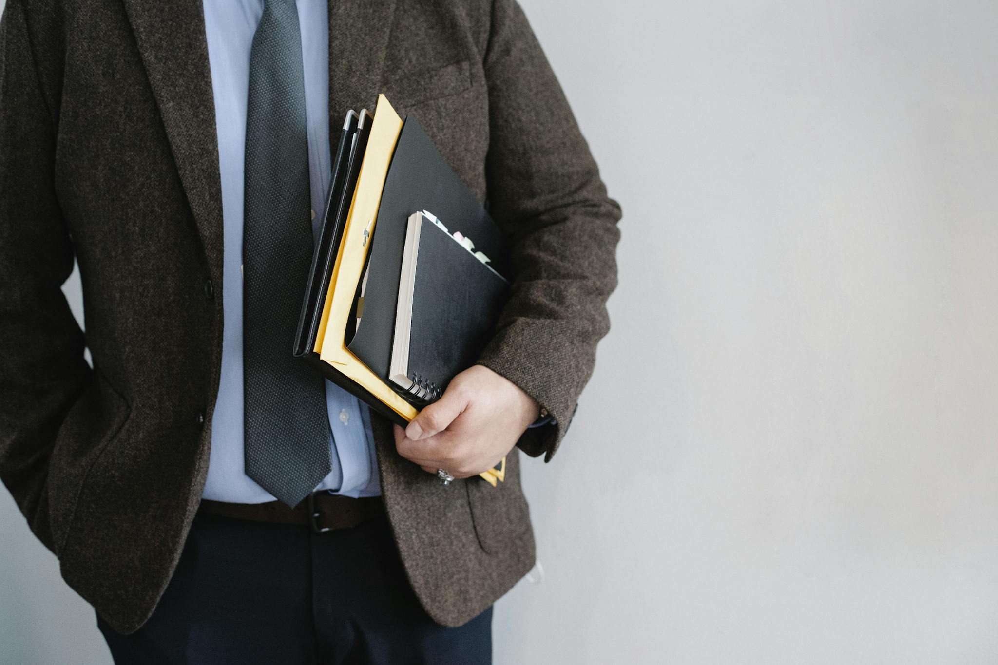 Business professional in a suit holding various folders and notebooks indoors.