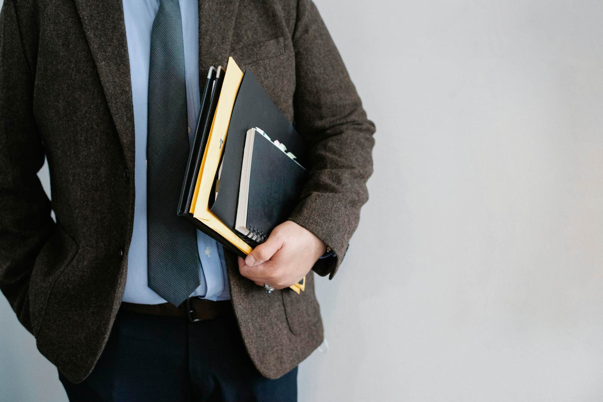 Business professional in a suit holding various folders and notebooks indoors.